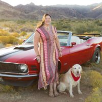 Jules Webb standing next to 1970 mustang convertible with Ryder, a yellow lab, with a desert background